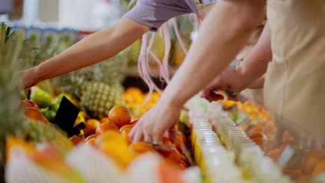 Primer-Plano-De-Una-Pareja-De-Trabajadores-De-Supermercado,-Un-Chico-Y-Una-Chica,-Colocando-Productos-En-El-Mostrador-De-Cítricos-En-Un-Supermercado.