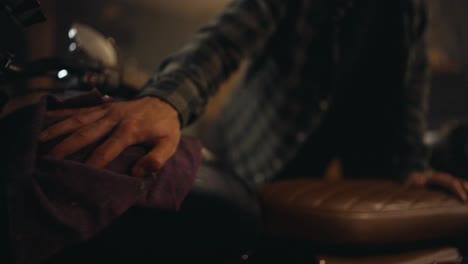 Close-up-a-guy-in-a-plaid-shirt-uses-a-rag-and-carefully-cleans-his-motorcycle-in-a-workshop