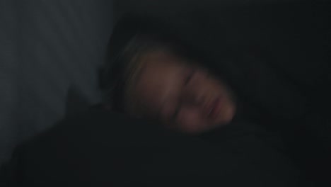 Portrait-of-a-blonde-girl-who-sharply-falls-her-head-in-bed-and-covers-herself-with-a-gray-blanket-at-night