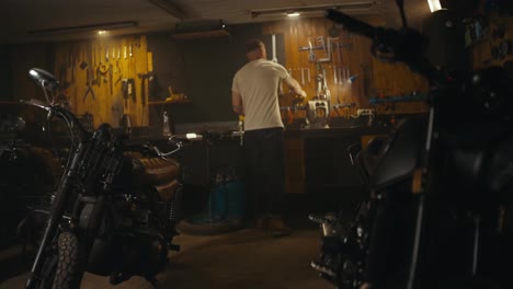 Blond-guy-in-a-white-T-shirt-mechanic-works-and-repairs-a-motorcycle-in-his-workshop