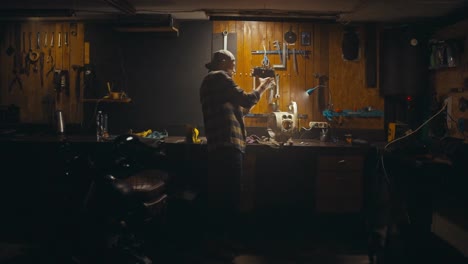 Side-view-of-a-mechanic-guy-in-a-cap-working-at-his-workbench-and-selecting-tools-in-a-cozy-studio-workshop