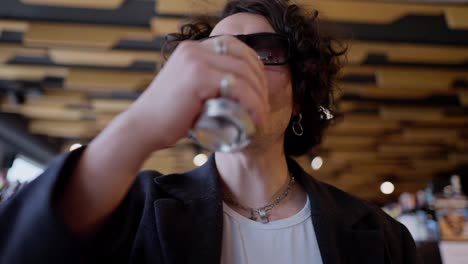 Confident-and-cool-guy-with-curly-black-hair-in-black-sunglasses-drinks-lemonade-and-wipes-his-mouth-with-his-hand-while-shopping-in-a-supermarket