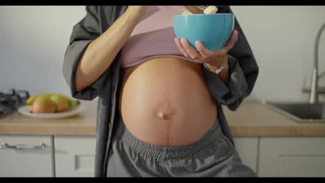 Retrato-De-Una-Mujer-Morena-Embarazada-Comiendo-Ensalada-De-Frutas-En-La-Cocina-En-El-Desayuno-De-La-Mañana.-La-Alimentación-Saludable-Durante-El-Embarazo-Es-La-Clave-Para-Un-Bebé-Sano.