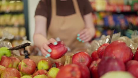 Close-up-of-a-girl-supermarket-worker-in-a-brown-T-shirt-and-apron-arranging-apples-on-the-counter-during-her-work-shift-at-the-supermarket