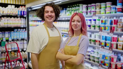 Porträt-Von-Supermarktmitarbeitern.-Ein-Brünetter-Mann-Und-Ein-Mädchen-Mit-Rosa-Haaren-Posieren-In-Der-Nähe-Der-Abteilung-Mit-Milchprodukten-Im-Supermarkt