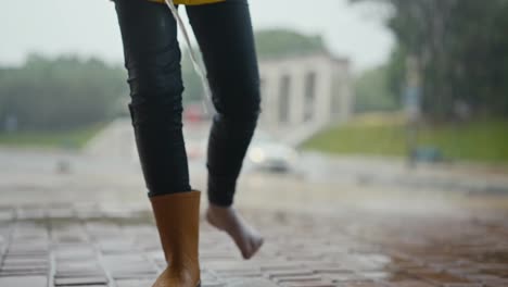 Close-up-of-a-teenage-girl-taking-off-her-orange-rubber-boots-and-draining-the-water-from-them-while-walking-and-raining-in-the-park