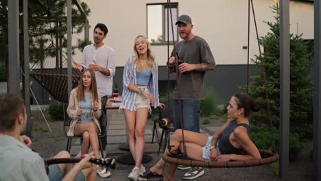 A-group-of-friends-relax-and-sing-while-their-friend-plays-the-guitar-in-the-courtyard-of-a-country-house-during-vacation