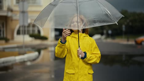 Blonde-teenage-girl-in-a-yellow-jacket-opens-an-umbrella-and-puts-out-her-hand-to-check-the-rain-while-walking-in-the-park