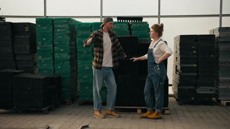 Guy-Farmer-with-a-beard-in-a-plaid-shirt-communicates-with-his-colleague-a-girl-with-red-hair-near-seedling-boxes-in-a-greenhouse-on-a-farm