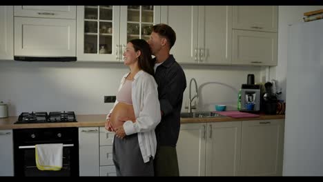 Happy-middle-aged-man-slow-dance-in-the-kitchen-with-his-pregnant-wife-while-relaxing-in-the-morning