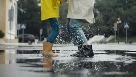 Nahaufnahme-Einer-Frau-In-Einer-Weißen-Jacke,-Die-Mit-Ihrer-Tochter-Bei-Einem-Spaziergang-Im-Park-Nach-Dem-Regen-In-Eine-Pfütze-Springt