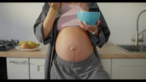 Close-up-of-a-pregnant-woman-eating-fruit-salad-from-a-blue-bowl-in-the-kitchen-in-the-morning-during-breakfast