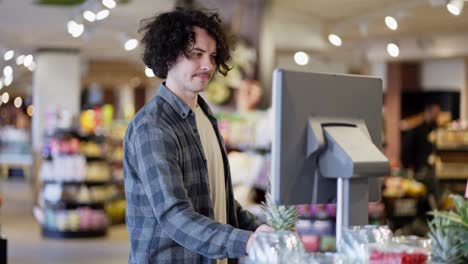 Un-Chico-Con-Pelo-Rizado-Y-Bigote-Con-Una-Camisa-A-Cuadros-Pesa-Una-Piña-En-Una-Báscula-En-Un-Supermercado.