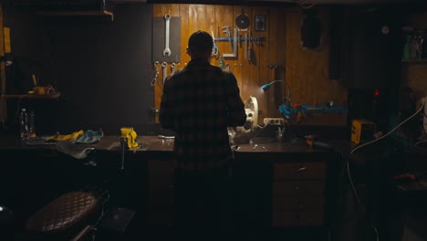 Rear-view-of-a-confident-guy-mechanic-working-on-his-workbench-and-picking-up-the-necessary-tools-from-the-rack-in-his-cozy-workshop