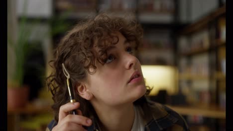 A-pensive-brunette-girl-with-curly-hair-looks-up-to-both-sides-while-thinking-at-the-table-in-the-library