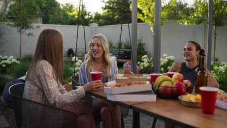 A-blonde-girl-eats-pizza-with-her-friends-and-chats-while-relaxing-at-a-table-in-the-courtyard-of-a-country-house