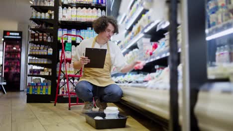 A-guy-with-curly-black-hair-takes-an-item-from-the-counter-and-checks-it-against-the-inventory-and-then-writes-off-the-expired-item-in-the-dairy-section-of-the-supermarket