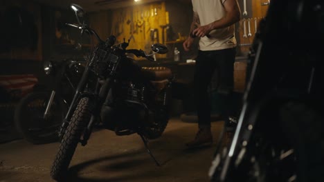 Confident-blond-guy-in-a-white-T-shirt-mechanic-works-and-repairs-a-motorcycle-in-his-workshop