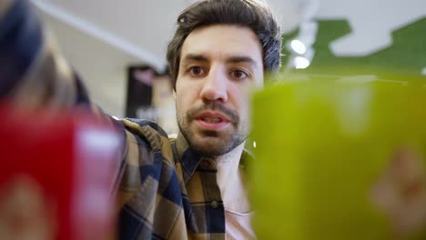 Close-up-a-confident-brunette-guy-with-stubble-in-a-checkered-shirt-chooses-the-products-he-needs-while-looking-at-a-supermarket-shelf