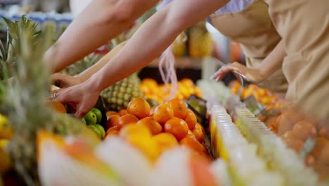 Close-up-a-guy-and-a-girl-supermarket-workers-sort-fruits-and-pineapples-orange-fruits-on-a-shelf-in-a-supermarket