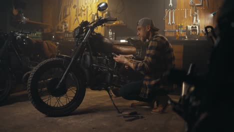 Side-view-of-a-confident-mechanic-in-a-plaid-shirt-inspecting-motorcycle-parts-during-repairs-in-his-workshop-studio