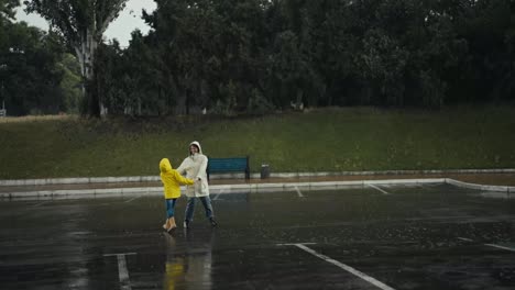 Happy-teenage-girl-in-a-yellow-jacket-dancing-with-her-mom-in-a-white-jacket-during-the-rain-in-the-park