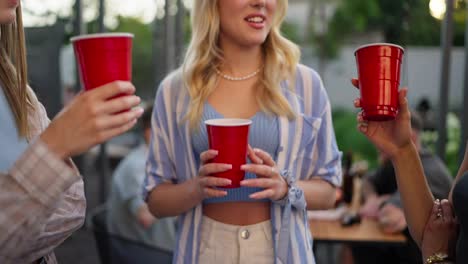 Close-up-a-trio-of-girls-holding-plastic-red-glasses-in-their-hands-communicate-and-have-fun-during-their-party-in-the-courtyard-of-a-country-house