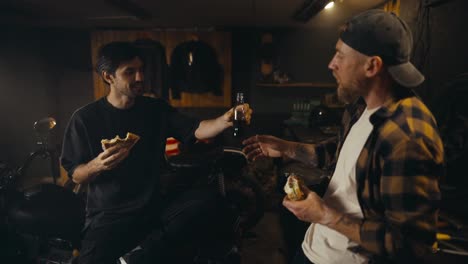 Un-Mecánico-Con-Camisa-A-Cuadros-Y-Su-Amigo-Comen-Una-Hamburguesa-Y-Beben-Refresco-Durante-Su-Almuerzo-En-Un-Taller.