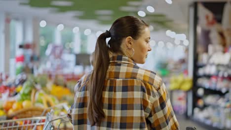 Rear-view-of-a-confident-brunette-girl-in-a-plaid-shirt-carries-her-small-child-in-her-arms-and-inspects-goods-in-a-supermarket-while-shopping