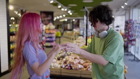 Close-up-of-a-girl-with-pink-hair-dancing-with-her-brunette-boyfriend-in-bright-clothes-while-shopping-in-a-grocery-store