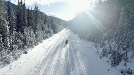 Drone-shot-of-a-snowmobile-riding-away-on-a-sunny-day