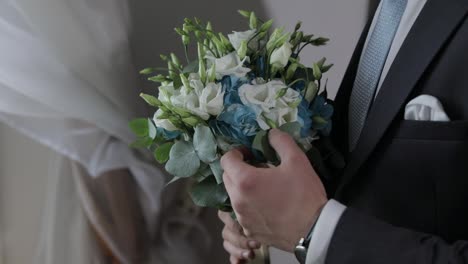 Groom-with-wedding-bouquet-in-his-hands-at-home.-White-shirt,-blue-tie,-jacket