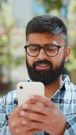 Indian-bearded-man-using-smartphone-typing-text-messages-in-social-media-application-online