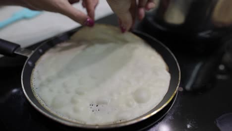 The-process-of-cooking-homemade-pancakes.-Woman-turns-pancake-in-a-frying-pan