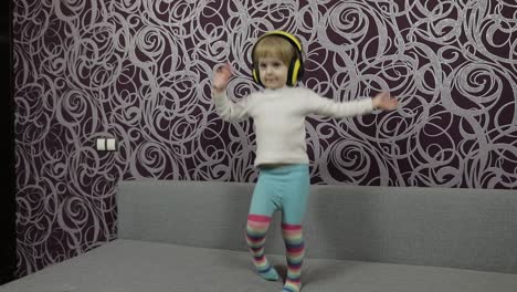 Little-happy-child-jumping-and-dancing-on-sofa-and-listening-music-in-headphones