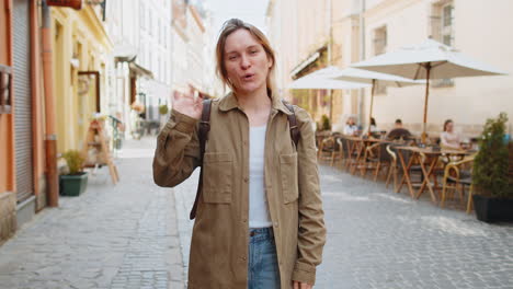 Girl-tourist-smiling-at-camera-waving-hands-gesturing-invitation-hello-greeting-on-city-street