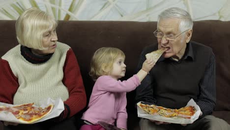 Beautiful-elderly-man-and-woman-eats-pizza-with-their-granddaughter