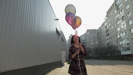 Pretty-woman-in-dress-holding-balloons-with-helium-outdoors-in-daylight