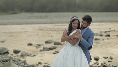 Wedding-couple-standing-near-mountain-river.-Groom-and-bride-in-love