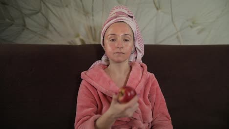 Woman-watching-a-late-night-movie-at-TV,-eating-an-apple.-Bathrobe,-facial-mask