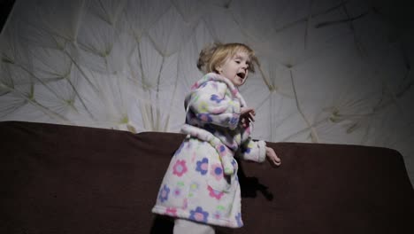 Little-cute-girl-with-blond-hair-jumps-on-sofa.-Bathrobe-clothes.-Happy