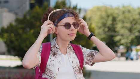 Portrait-of-happy-smiling-tourist-young-man-listening-music-taking-off-headphones-looking-at-camera