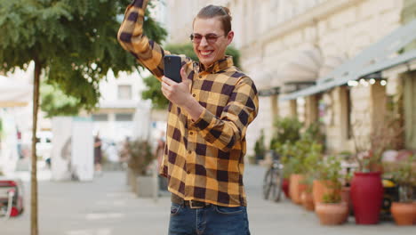 Happy-man-using-mobile-smartphone-on-city-street-celebrating-win-good-email-message-news-victory