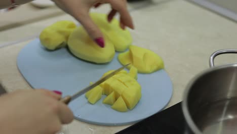 Woman-cutting-potato-on-the-blue-cutting-board