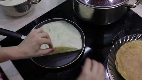 The-process-of-cooking-homemade-pancakes.-Woman-turns-pancake-in-a-frying-pan