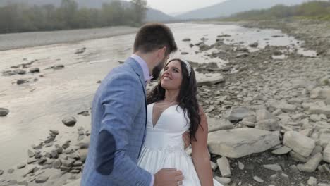 Wedding-couple-standing-near-mountain-river.-Groom-and-bride-in-love