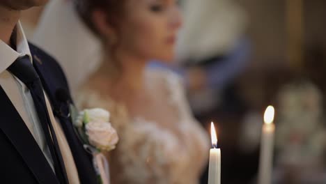 The-bride-and-the-groom-stand-in-church,-holding-candles-in-their-hands