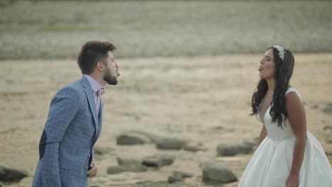 Wedding-couple-standing-near-mountain-river.-Groom-and-bride-making-faces