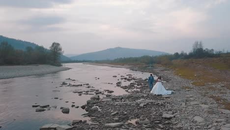 Wedding-couple-stand-near-mountain-river.-Groom-and-bride.-Arial-view