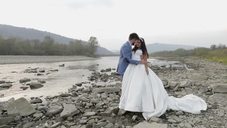 Wedding-couple-standing-near-mountain-river.-Groom-and-bride-in-love